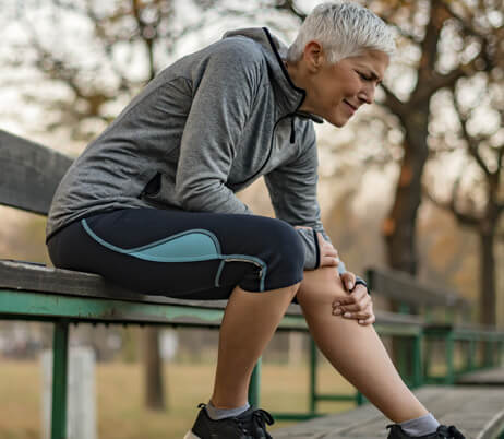 Woman suffering cartilage tears in her knee sitting on a park bench and holding her knee in pain.