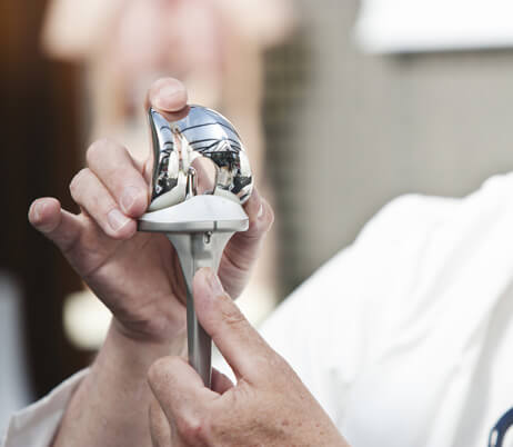 Top knee replacement surgeon in Naples, FL, holding a metal prosthetic knee.