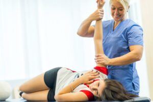 A female orthopedic surgeon is helping a female athlete with shoulder pains, probably from rotator cuff injuries.