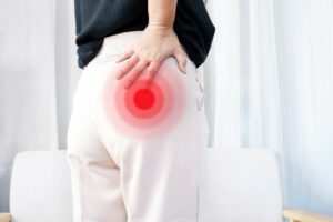 A woman wearing white pants is suffering from hip pain while holding her hip.
