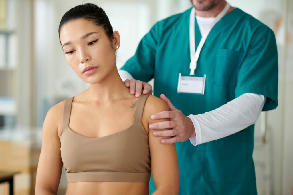 A therapist palpates the shoulder of a sportswoman experiencing shoulder pain and tendonitis during a physical therapy session.