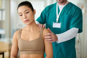 A therapist palpates the shoulder of a sportswoman experiencing shoulder pain and tendonitis during a physical therapy session.