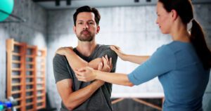 A female physiotherapist is guiding a man through physical therapy and shoulder exercises for his shoulder tendonitis.