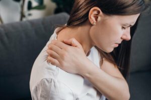 A woman is massaging her stiff, sore shoulder to relieve tense, fatigued muscles caused by shoulder pain.