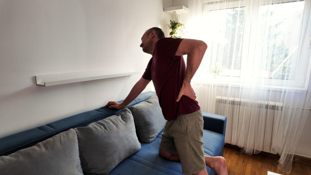 A man is holding his hip and back due to experiencing sciatica pain at home.