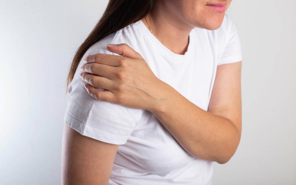 A girl in a white T-shirt is holding her shoulder joint and is in severe shoulder pain.