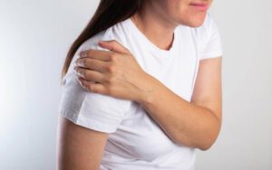 A girl in a white T-shirt is holding her shoulder joint and is in severe shoulder pain.