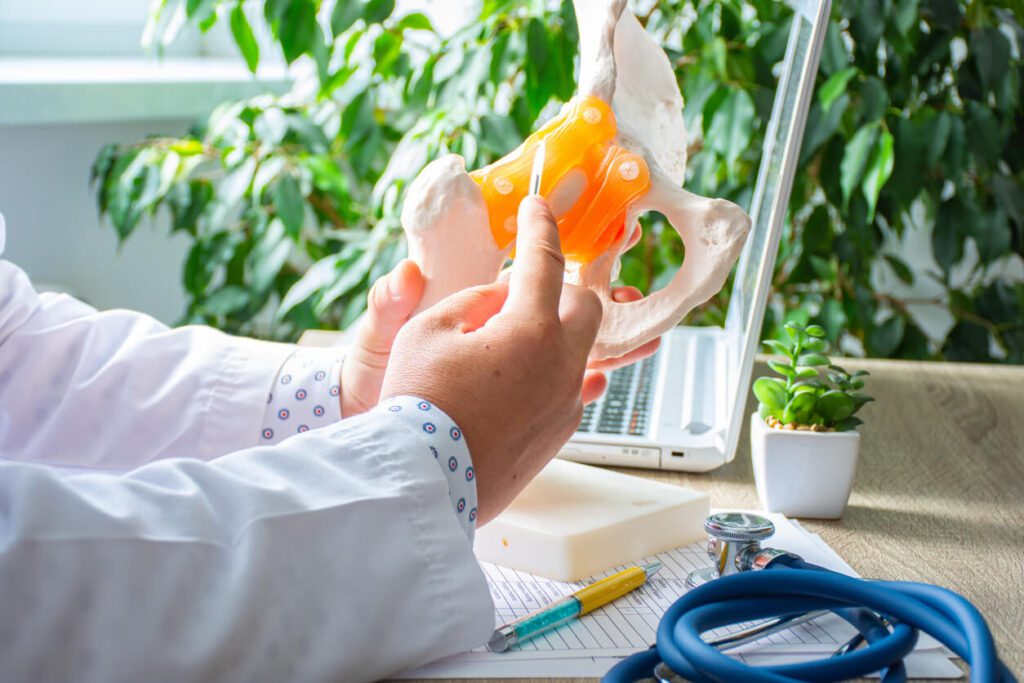 Doctor holds the scalpel over the anatomical model of the hip joint and shows the patient how hip resurfacing procedure looks like.